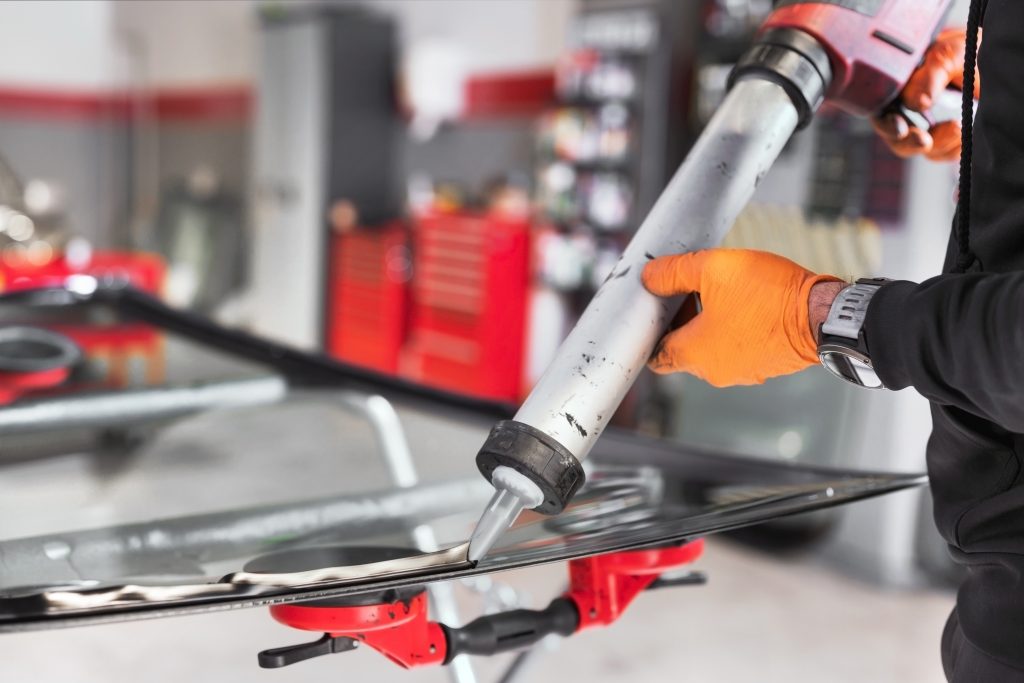 glazier,applying,rubber,sealing,to,windshield,in,garage,,close,up.